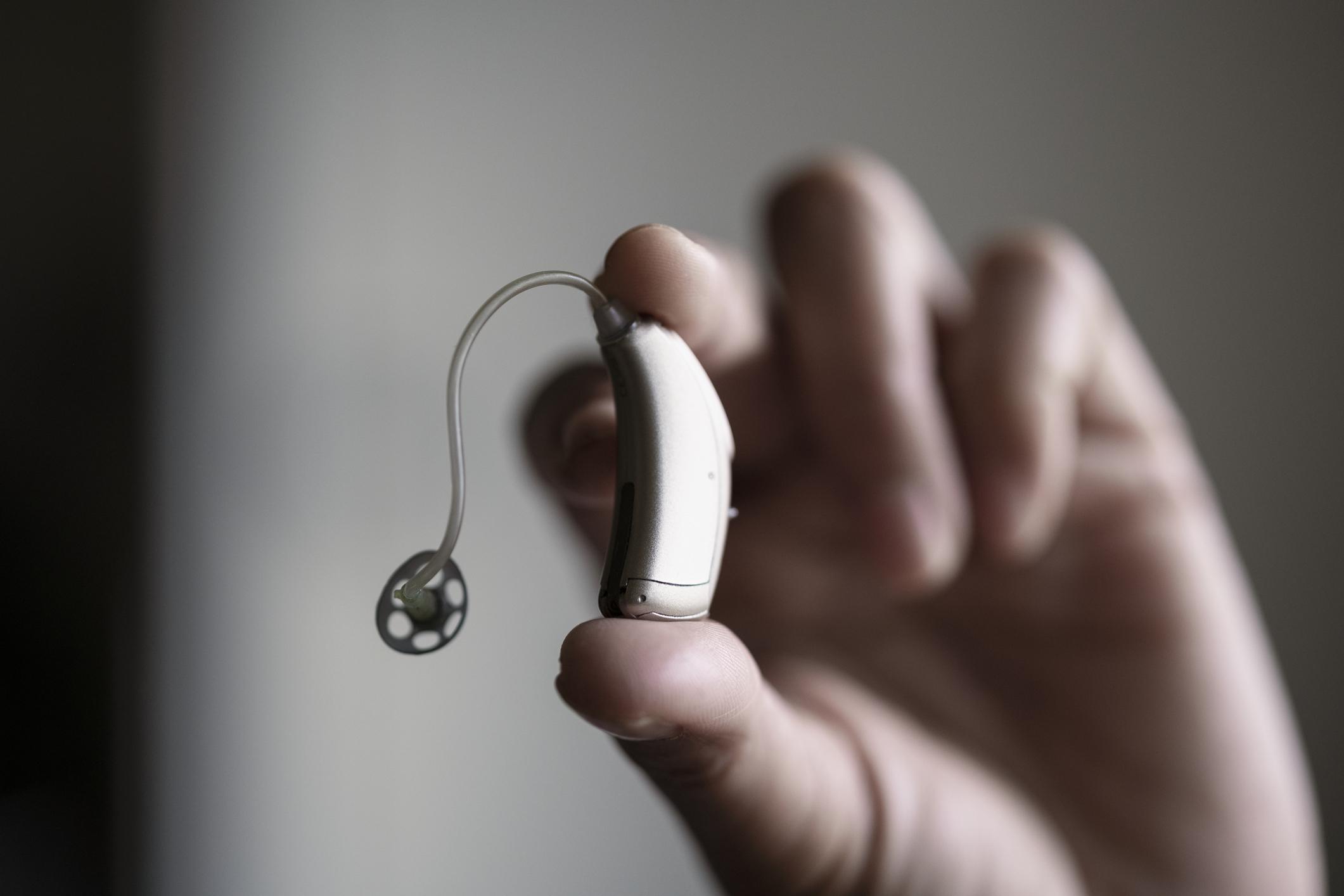 Esco Hearing Aid Protection A close-up of a person's fingers holding a modern, behind-the-ear hearing aid.