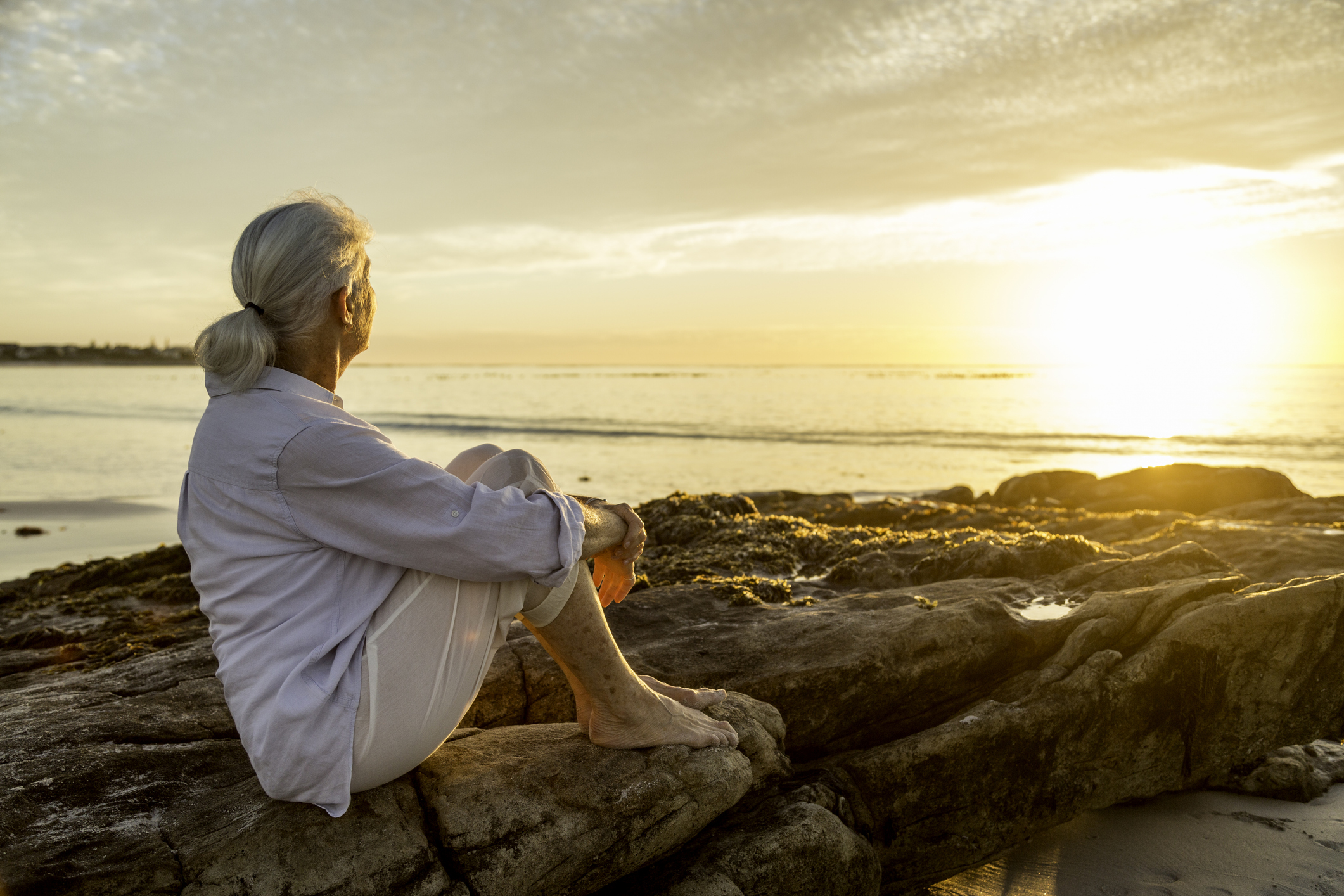 Senior woman relaxing by the ocean at sunset Senior woman relaxing by the ocean at sunset, representing the peace of mind that comes with understanding your hearing aid warranty coverage.